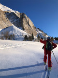 Skieur montant dans une prairie enneigée devant une falaise